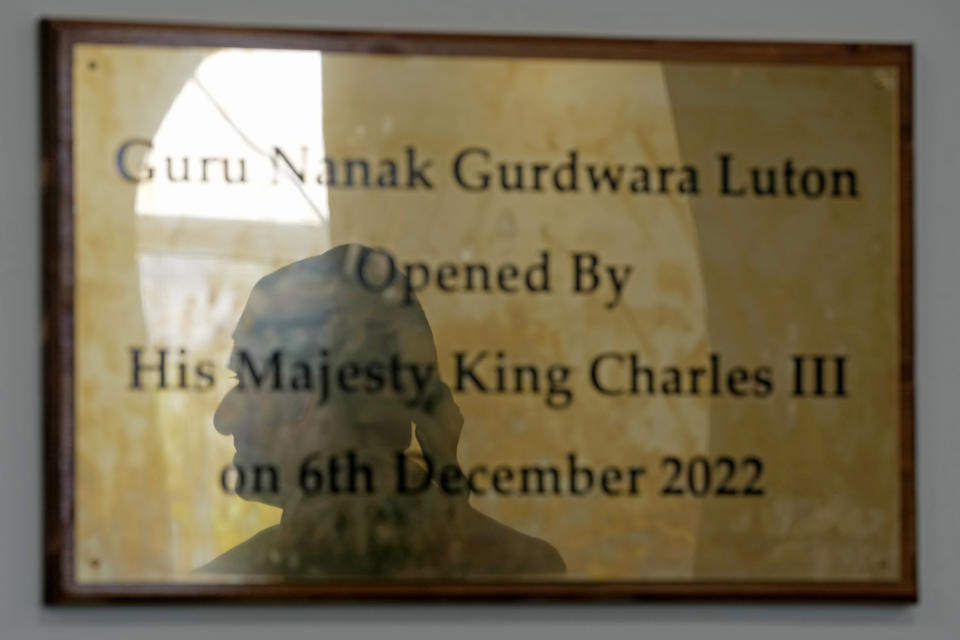 The shadow of Gurch Randhawa is reflected in a plaque commemorating King Charles III's visit to the Guru Nanak Gurdwara in Luton, England, in a photo taken on Thursday, April 27, 2023. King Charles III visited the Sikh house of worship last year as part of his efforts to build bridges with faith groups and show that the monarchy, a 1,000-year-old institution with Christian roots, can still represent the people of modern, multi-cultural Britain. (AP Photo/Kin Cheung)