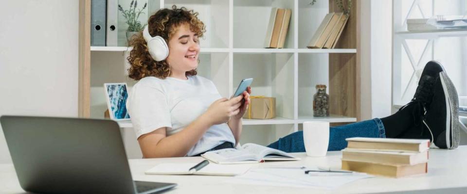 Gadget people. Indoors leisure. Phone browsing. Mobile communication. Satisfied overweight curly hair woman student in headphones typing message at modern light apartment.