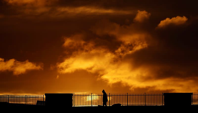 Man walks his dog as the sun rises over the Irish Sea fishing village of Carnlough