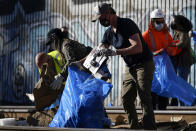 California Governor Gavin Newsom, center, removes cardboard and other discarded items from a Union Pacific railroad site on Thursday, Jan. 20, 2022, in Los Angeles. Gov. Gavin Newsom on Thursday promised statewide coordination in going after thieves who have been raiding cargo containers aboard trains nearing downtown Los Angeles for months, leaving the tracks blanketed with discarded boxes. (AP Photo/Ashley Landis)