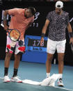 Russia's Karen Khachanov, right, and Australia's Nick Kyrgios dry the court with a towel during their third round singles match at the Australian Open tennis championship in Melbourne, Australia, Saturday, Jan. 25, 2020. (AP Photo/Lee Jin-man)