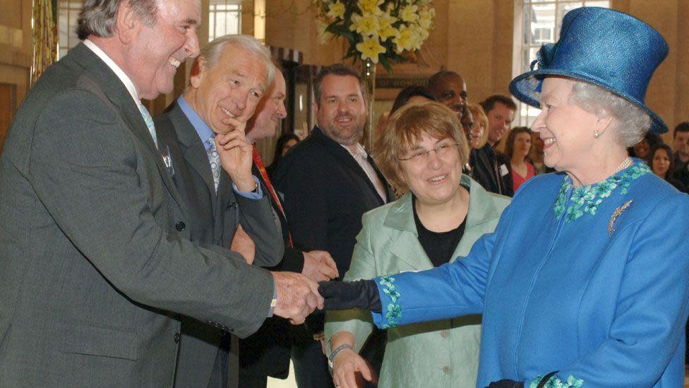 Dame Jenny Ambramsky introduces Elizabeth II, who is wearing a blue coat and hat, to radio presenters