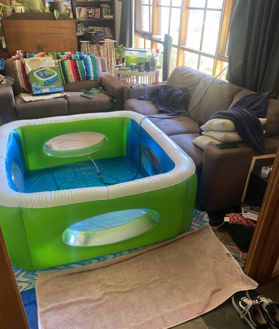 A blow up pool being filled with a hose inside a living room.