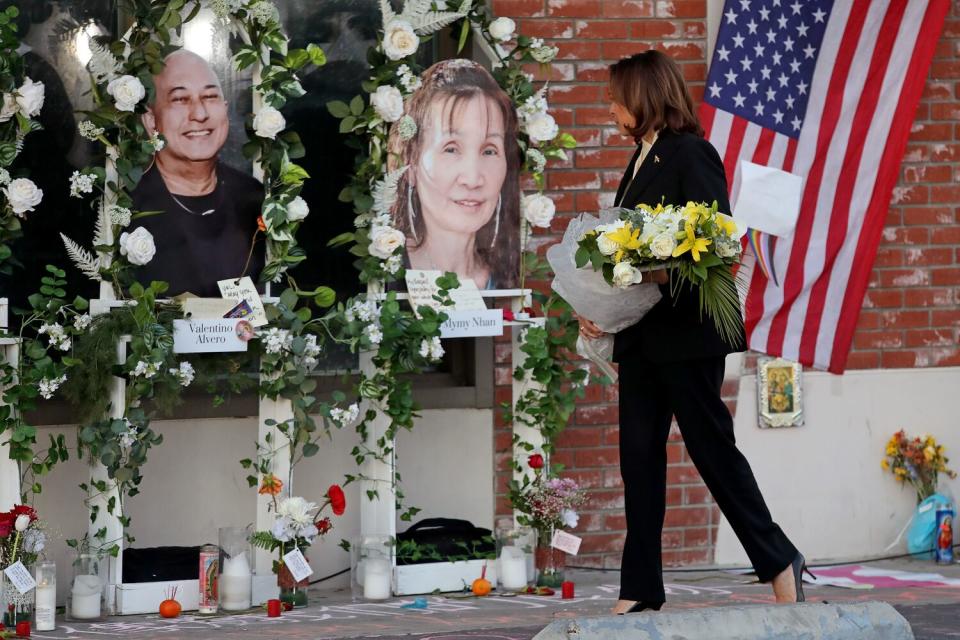 Vice President Kamala Harris carries a wreath while walking in front of portraits of shooting victims