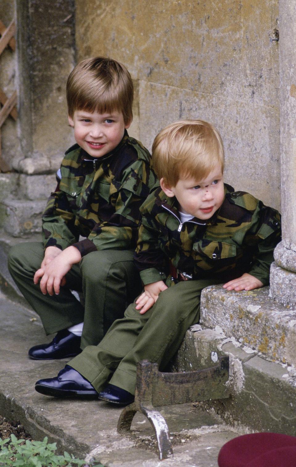 Prince Harry and Prince William sit together on the steps of Highgrove House wearing army uniforms on July 18, 1986 in Tetbury, England.