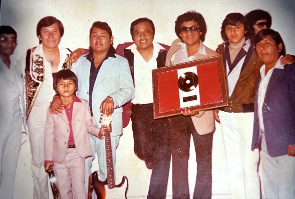 old photo of eight men with arms around each other, one holding an award, and a child