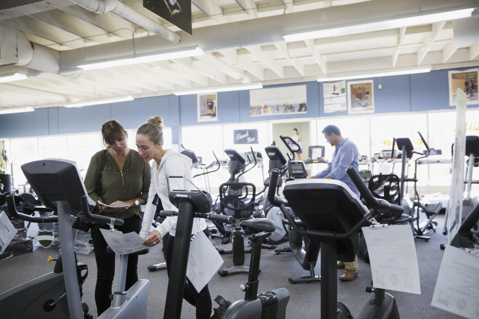 Saleswoman helping woman browsing cardio machines at home gym equipment store