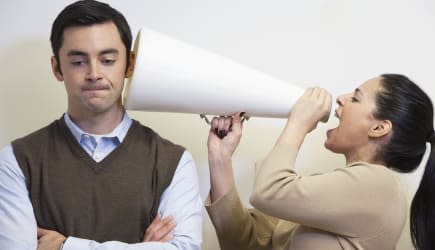 Businesswoman shouting with megaphone into co-worker&#39;s ear