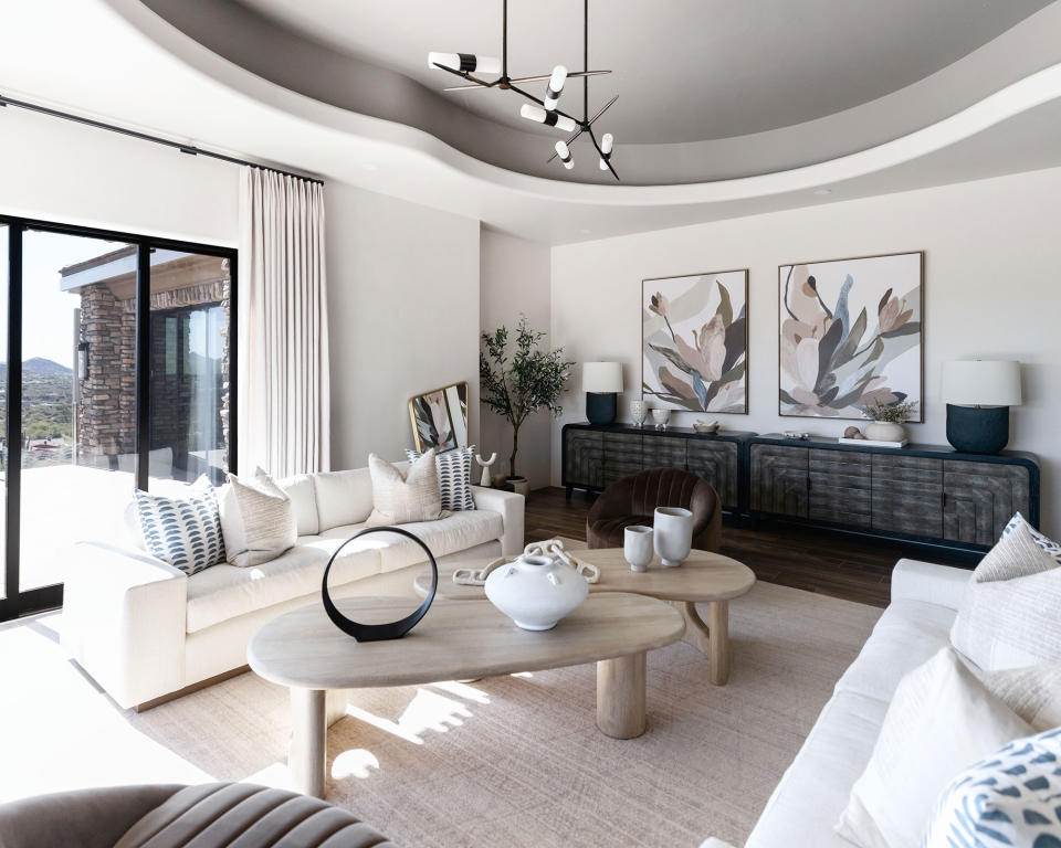 Minimal neutral living room with art on walls, circular coffee tables, accent pendant light, and cream couches