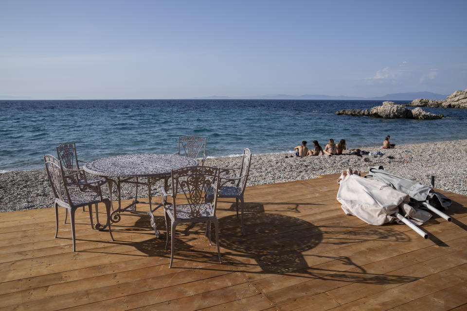 People sit on at a beach in Kokkari , in front of a tavern on the eastern Aegean island of Samos, Greece, Tuesday, June 8, 2021. About a month after Greece officially opened to international visitors, the uncertainty of travel during a pandemic is still taking its toll on the country's vital tourist industry. (AP Photo/Petros Giannakouris)