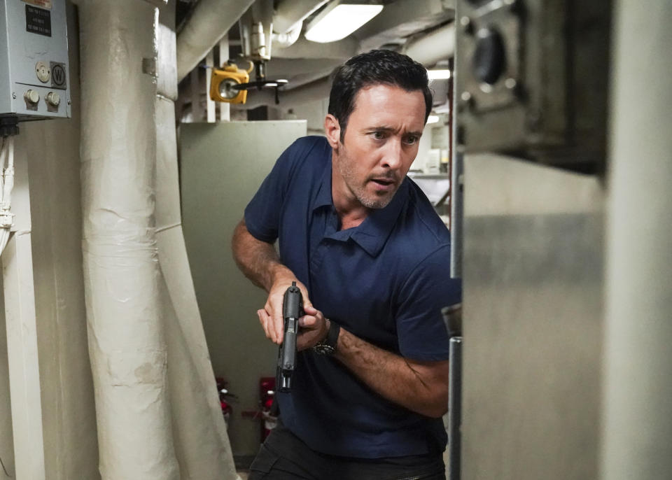 A tense scene with Alex O'Loughlin holding a gun, ready to take action in an industrial setting