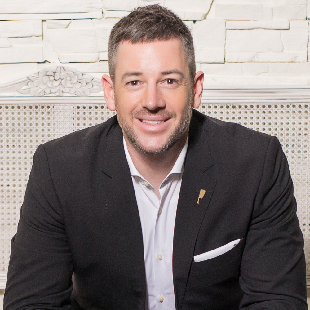 Headshot of business coach Daniel Tolson in a suit on a pale background