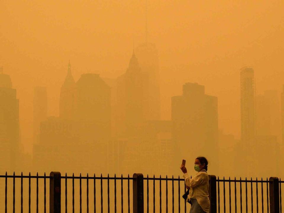 A person wearing a face mask takes photos of the skyline as smoke from wildfires in Canada cause hazy conditions in New York City on June 7, 2023.