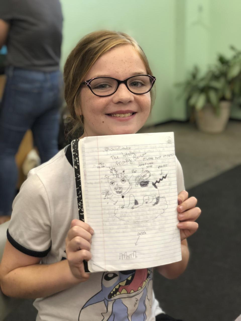 In this June 8th, 2018 photo provided by Syed Ali Haider, 10-year-old Genevieve Thiel shows off her work during Austin Bat Cave's week-long Magical Realism summer camp in Austin, Texas. Educators say teaching critical and creative writing is just as important as strong reading and is too often overlooked. "When students own their voices and tell their stories, they become not only stronger and more confident writers, but also stronger and more confident individuals," says Ali Haider, executive director of Bat Cave, the Austin-based creative writing center. (Syed Ali Haider via AP)