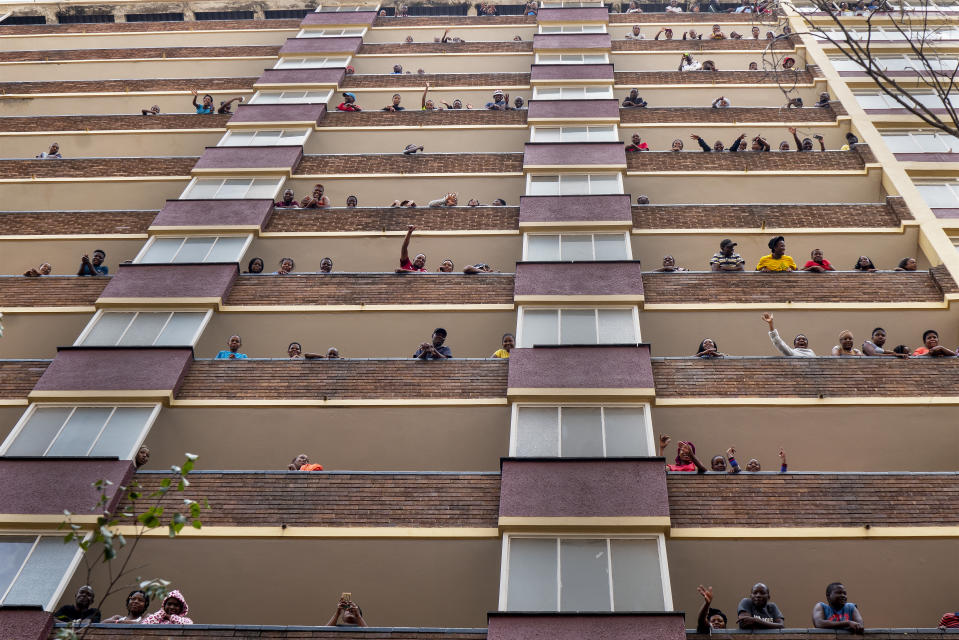 Residents of the densely populated Hillbrow neighborhood of downtown Johannesburg, confined in an attempt to prevent the spread coronavirus, stand and wave from their balconies, Friday, March 27, 2020. South Africa went into a nationwide lockdown for 21 days in an effort to mitigate the spread to the coronavirus. The new coronavirus causes mild or moderate symptoms for most people, but for some, especially older adults and people with existing health problems, it can cause more severe illness or death. (AP Photo/Jerome Delay)