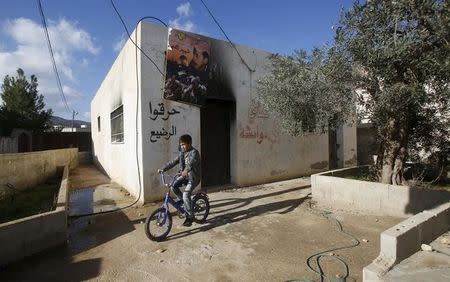 A Palestinian boy rides his bicycle past the Dawabsheh family house near the West Bank city of Nablus, December 3, 2015. REUTERS/Abed Omar Qusini/Files