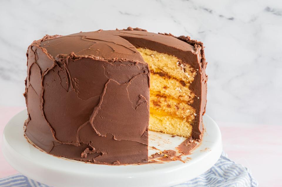 a layer cake covered in chocolate frosting with a slice cut out to reveal yellow layers