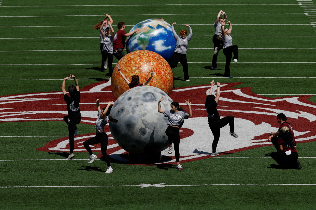 People dance next to representations of the Earth, sun and moon at Saluki Stadium, ahead of a total solar eclipse, in Carbondale, Ill.