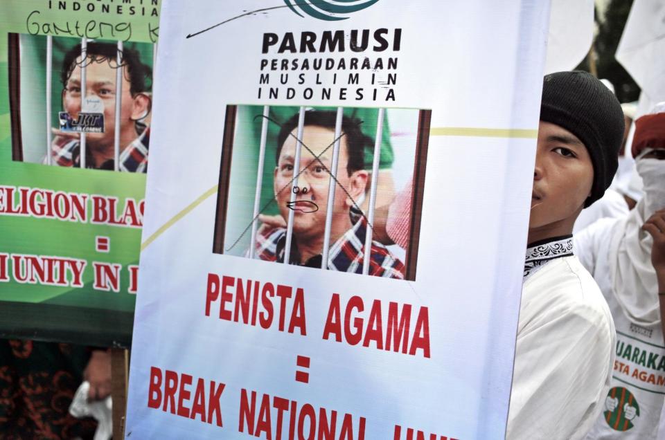A Muslim man displays a poster during a protest against Jakarta Governor Basuki "Ahok" Tjahaja Purnama outside the North Jakarta Court where his blasphemy trial is held, in Jakarta, Indonesia, Tuesday, Dec. 27, 2016. The court ruled Tuesday that the blasphemy trial of the minority Christian governor who is charged with insulting Islam and desecrating the Quran will proceed. Writings on the poster reads: "Blasphemer = breaking national unity." (AP Photo/Dita Alangkara)