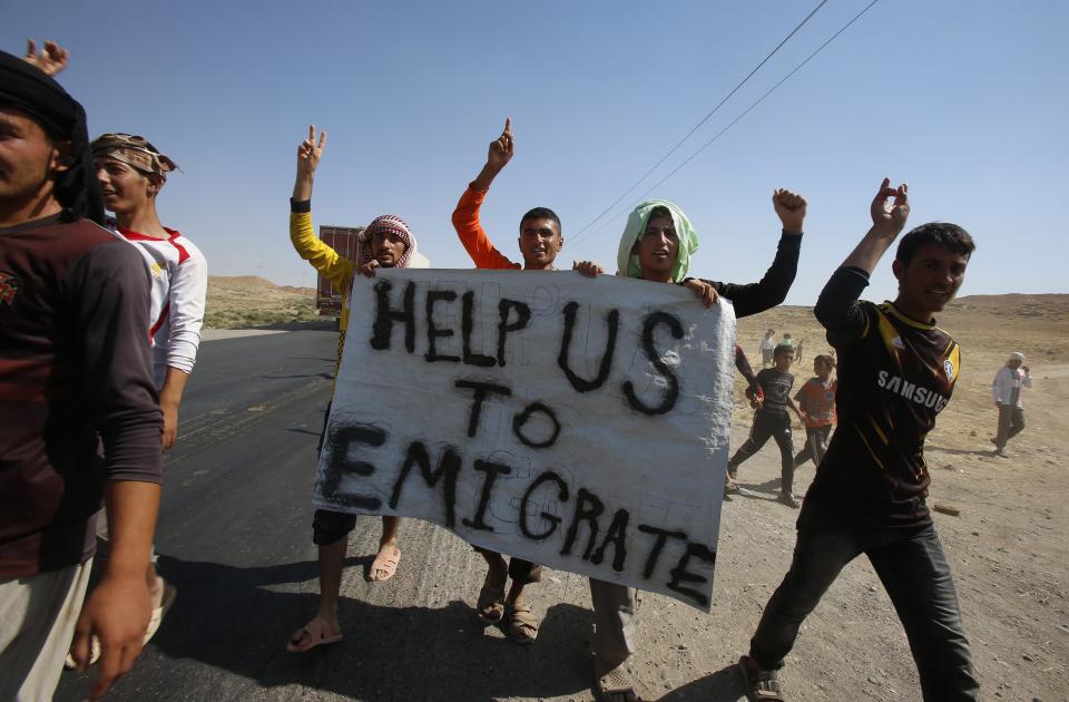 Displaced people from the minority Yazidi sect, who fled the violence in the Iraqi town of Sinjar, hold a banner as they take part in a demonstration at the Iraqi-Syrian border crossing in Fishkhabour, Dohuk province August 13, 2014. Demonstrators demanded protection and evacuation from Iraq to safer areas such as Europe and the United States. REUTERS/Youssef Boudlal (IRAQ - Tags: CIVIL UNREST POLITICS)