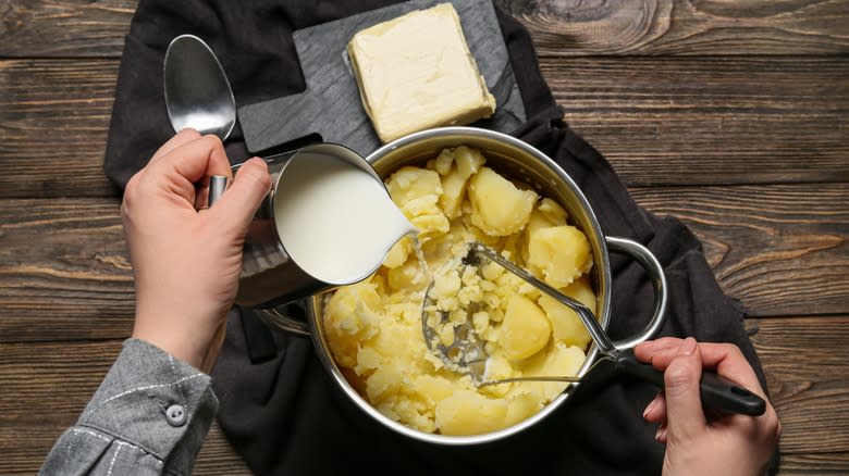 person pouring milk into mashed potatoes