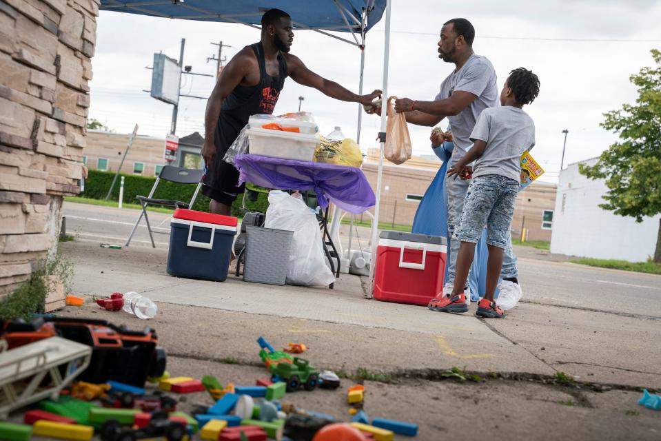 Myron Banks, 34, left, hands food to customer Robert Thomas, 30, of Detroit, as his son Royal Banks, 6, stands near their barbecue tent on East Warren Avenue in Detroit's Cornerstone Village neighborhood on Thursday, July 13, 2023. "I've been doing this for four years now and most of the people in the area know me," said Banks. "I'm one of the best street barbecuers."