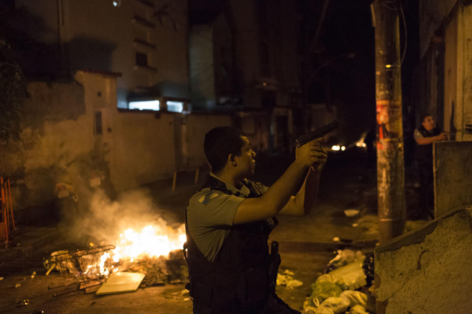 Officers of the Police Pacification Unit patrol next to a burning barricade during clashes at the Pavao Pavaozinho slum in Rio de Janeiro, Brazil, Tuesday, April 22, 2014. Intense exchanges of gunfire, numerous blazes set alite and a shower of homemade explosives and glass bottles onto a busy avenue in Rio de Janeiro’s main tourist zone erupted Tuesday night after the death of a popular young shantytown resident. (AP Photo/Felipe Dana)