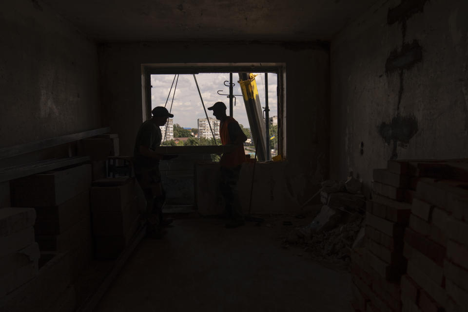 Two construction workers carry building materials in an apartment badly damaged in Russian attacks in Borodyanka, Ukraine, Wednesday, Aug. 2, 2023. Borodyanka was occupied by Russian troops at the beginning of their full-scale invasion last year. (AP Photo/Jae C. Hong)
