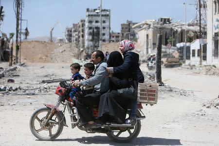 A family rides on a motorbike along a damaged street in the city of Douma, Damascus, Syria April 16, 2018. REUTERS/Ali Hashisho