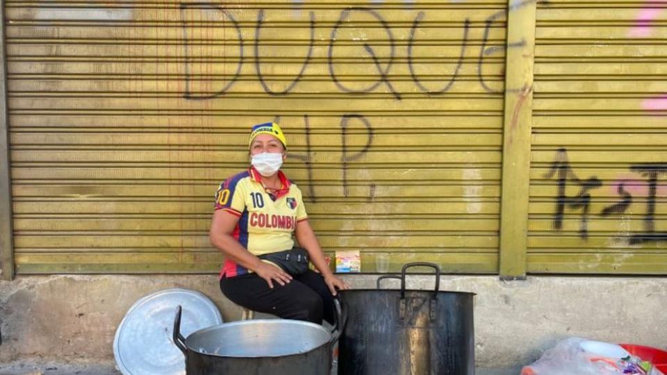 Una señora en Cali. A sus espaldas una valla pintada con las palabras "Duque HP".