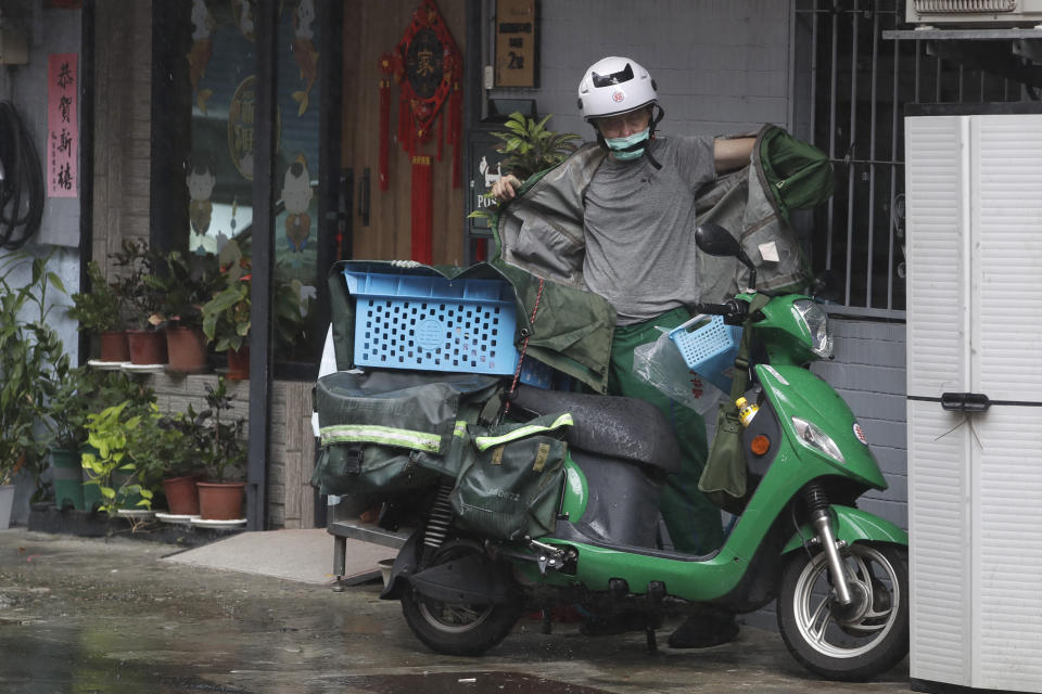 A postman takes a shelter from a heavy rain under the eaves after Typhoon Saola moves away in Taipei, Taiwan, Thursday, Aug. 31, 2023. (AP Photo/Chiang Ying-ying)