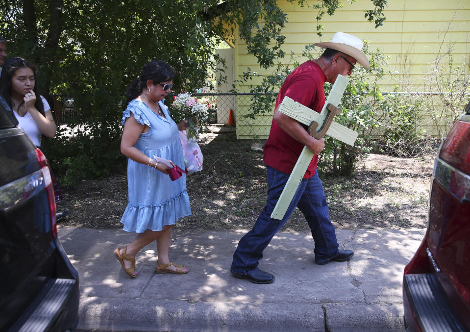 A man carries a cross he made as his wife, carries flowers to pay their respects to the 21 victims of the Robb Elementary School shooting in Uvalde, Texas on Thursday, May 26, 2022. (Kin Man Hui/The San Antonio Express-News via AP)