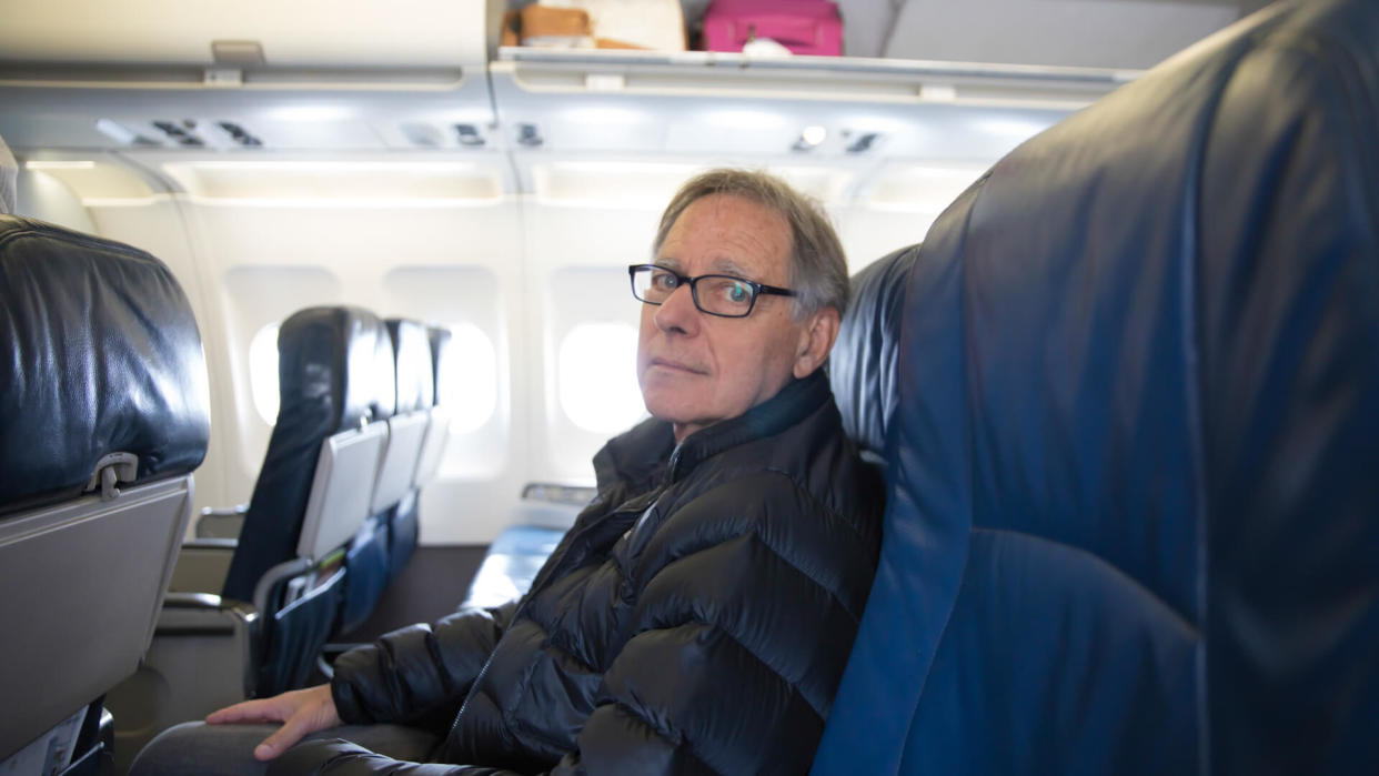 Senior male is sitting in his seat on a airplane waiting for his flight to depart.