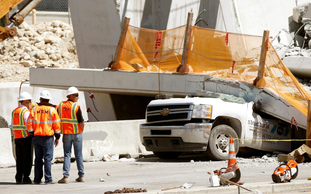 Workers stand next to a section of a collapsed pedestrian bridge near Florida International University in the Miami area - AP