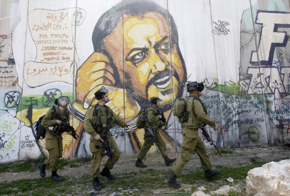 FILE - In the background of part of Israel's separation barrier with portrait of jailed Fatah leader Marwan Barghouti, Israeli soldiers patrol at Kalandia checkpoint between Jerusalem and the West Bank city of Ramallah, Thursday, March 8, 2012. Hamas officials say that any cease-fire deal with Israel should include the release of prisoner Marwan Barghouti — a leader of the militant group's main political rival. The demand by Hamas marks the central role Barghouti plays in Palestinian politics — even after more than two decades behind bars and sentenced by Israel to multiple life terms in prison. (AP Photo/Nasser Shiyoukhi, File)