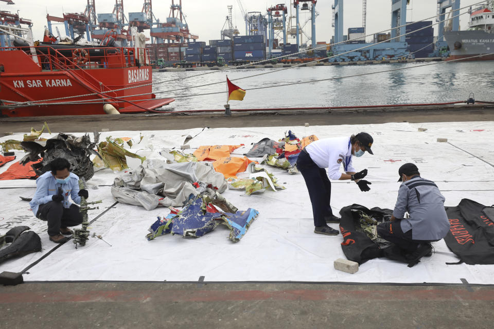 Investigators of the National Transportation Safety Committee inspect parts of aircraft's debris recovered from the Java Sea where a Sriwijaya Air passenger jet crashed, at Tanjung Priok Port, Tuesday, Jan. 12, 2021. Indonesian navy divers were searching through plane debris and seabed mud Tuesday looking for the black boxes of the Sriwijaya Air jet that nosedived into the Java Sea over the weekend with 62 people aboard. (AP Photo/Dita Alangkara)