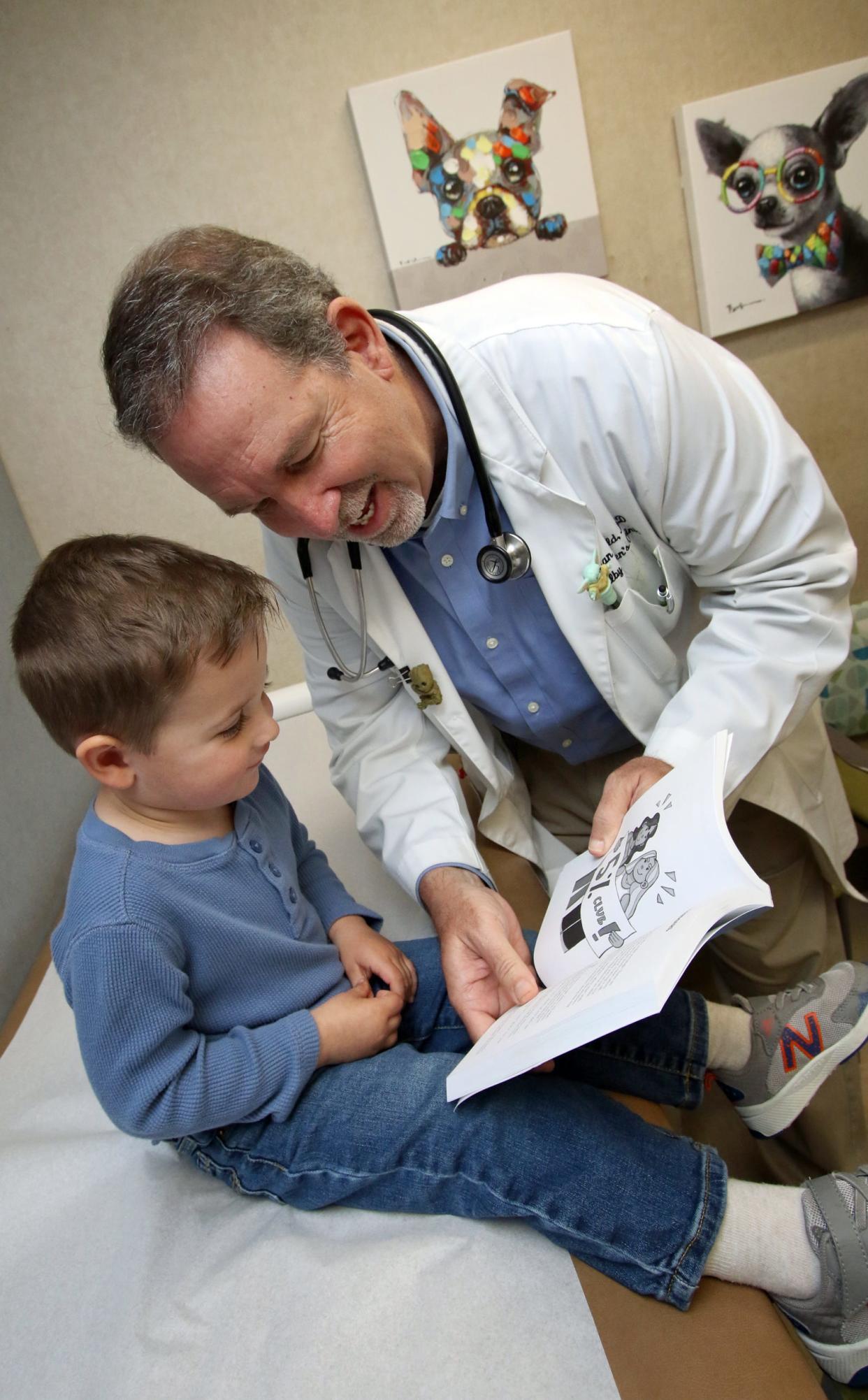 Dr. Brian Benfield shows his book to three-year-old Huxley Falls Tuesday morning, March 26, 2024, at the Atrium Health Levine Children's Shelby Children's Clinic.