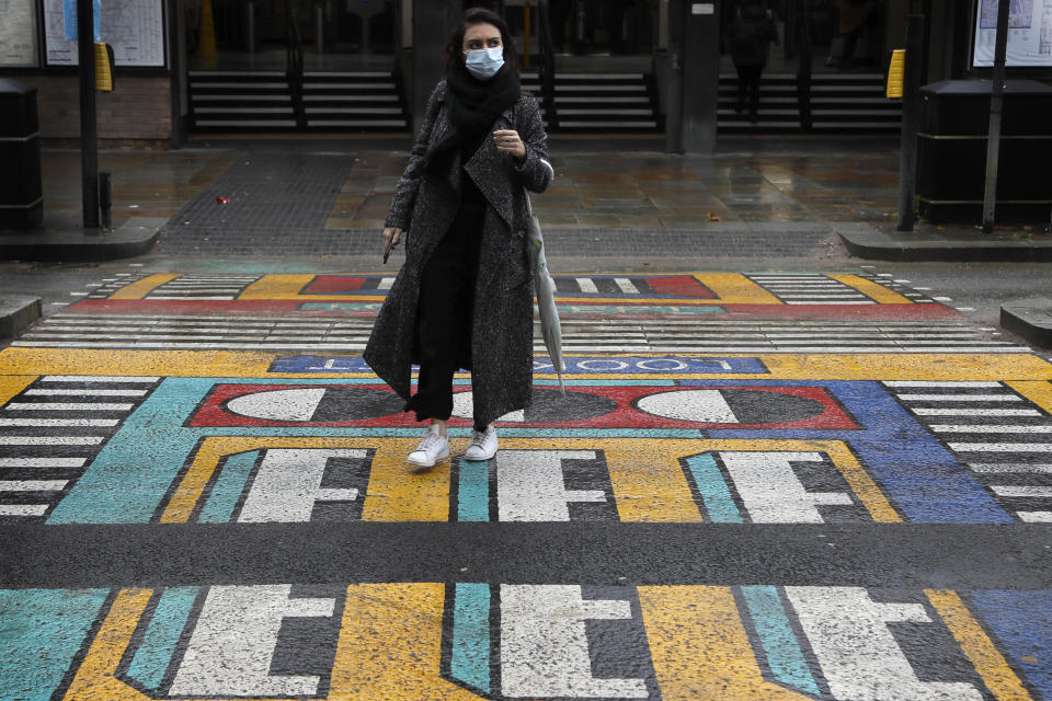 A woman walks over a pedestrian crossing, part of a public artwork by French artist Camille Walala, in London, Tuesday, Oct. 27, 2020. The British government is sticking to its strategy of tiered, regional restrictions to combat COVID-19 amid mounting political and scientific pressure for stronger nationwide measures to prevent the pandemic from spiralling out of control. (AP Photo/Kirsty Wigglesworth)