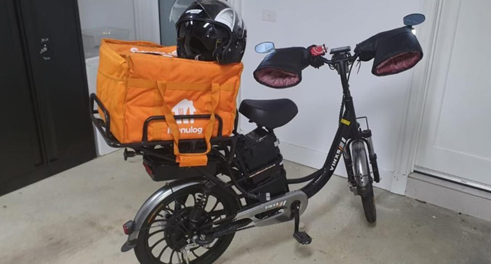 Black e-bike with orange Menulog bag. 
