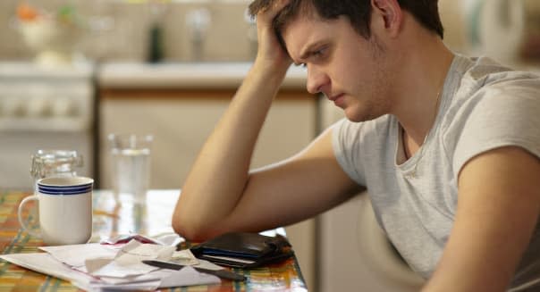 Young man holding head looking at receipts.