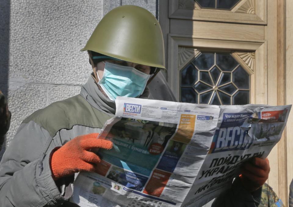 An Ukrainian government supporter reads a news paper as he guards Ukrainian parliament building in Kiev, Ukraine, Tuesday, March 11, 2014. Ukrainian Prime Minister Arseniy Yatsenyuk on Tuesday reiterated his call for Western nations to defend Ukraine against Russia.(AP Photo/Efrem Lukatsky)