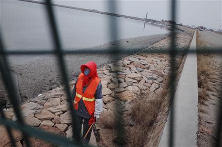 A cleaner wearing a mask is seen behind a barrier next to leaked oil after an explosion at a Sinopec Corp oil pipeline in Huangdao, Qingdao, Shandong Province November 23, 2013. REUTERS/Mo Yat