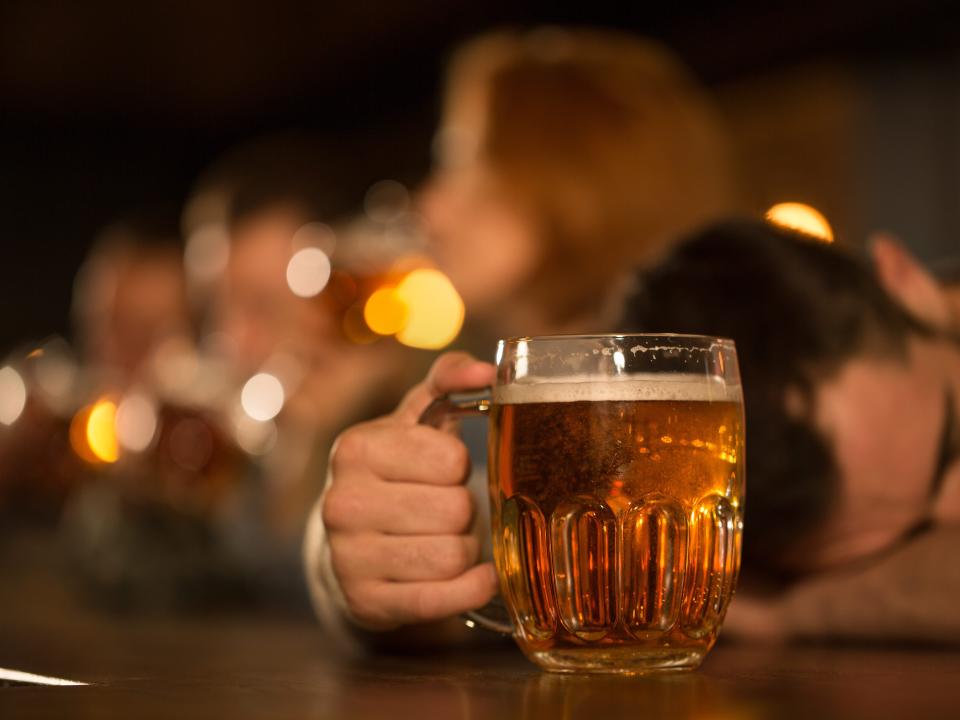 A drunk man passed out behind his beer at a bar.