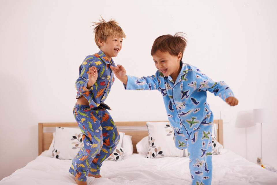 Two young boys jump on a bed in their pajamas