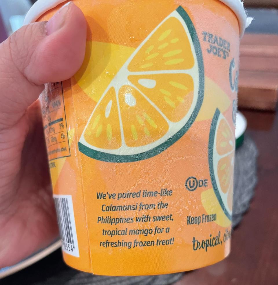 Hand holding a Trader Joe's frozen treat with lime and calamansi fruit graphics. Text: "We've paired lime-like Calamansi from the Philippines with sweet, tropical mango for a refreshing frozen treat!"