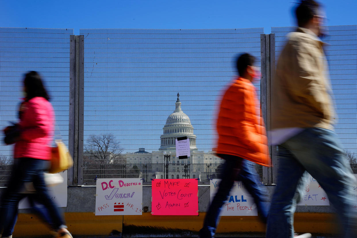 People walk past signs hung on a security fence in support of expanded voting rights near the U.S. Capitol in Washington