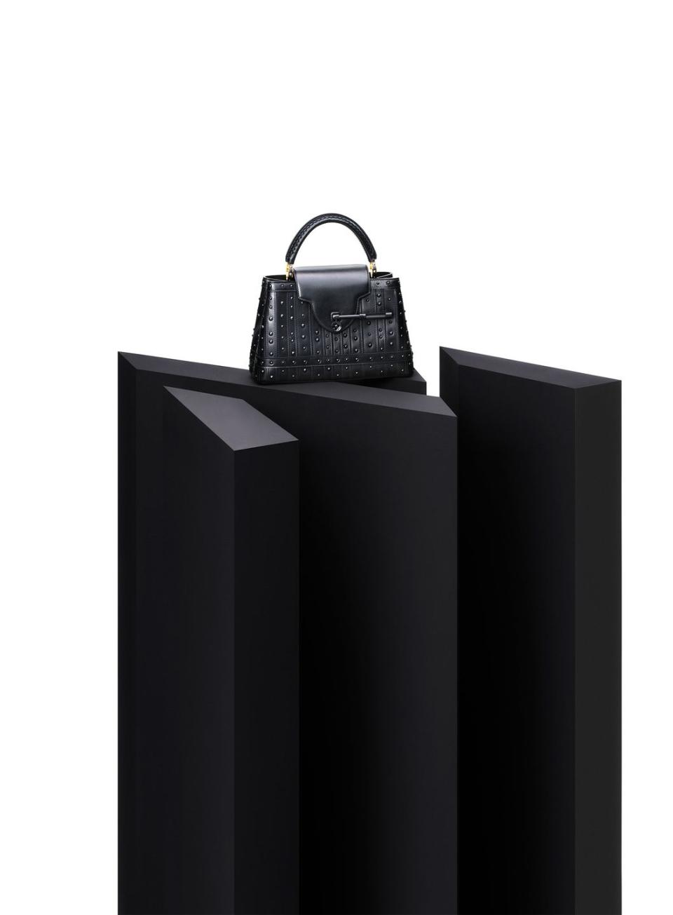 black handbag with studs and short handle on a black pedestal