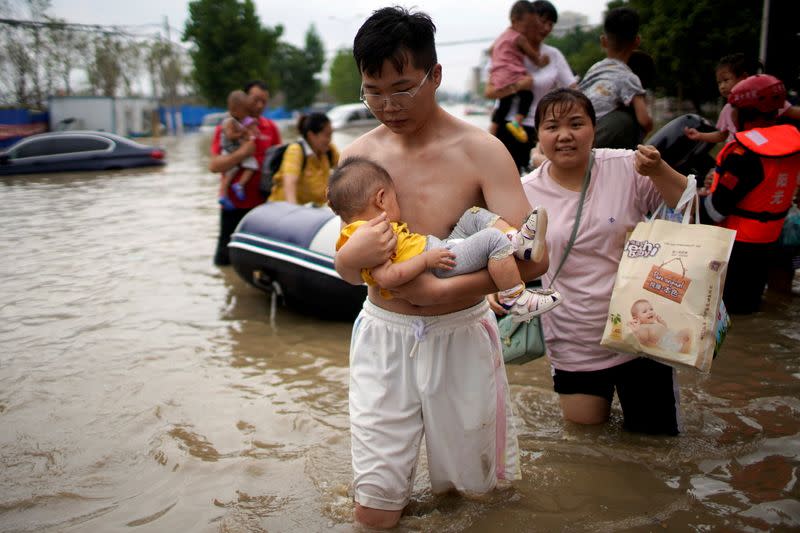 FILE PHOTO: Man holding a baby wades through a flooded road following heavy rainfall in Zhengzhou