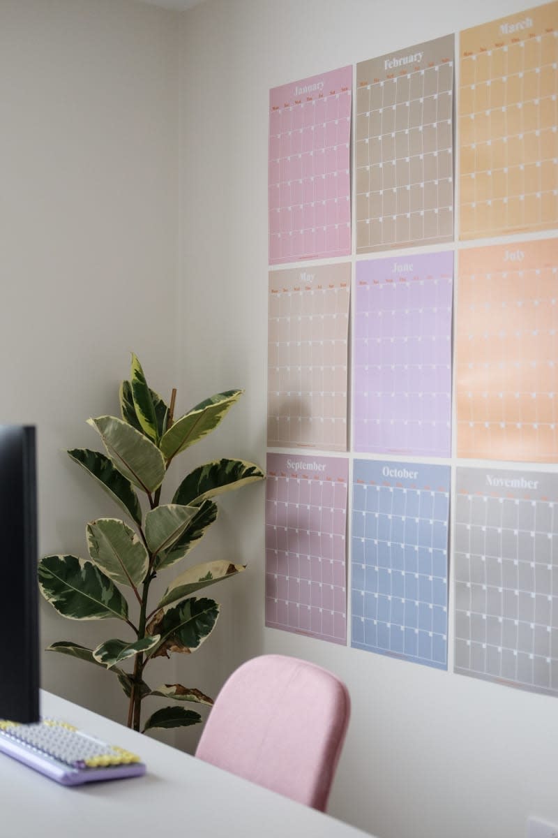 large colorful calendar pages on wall behind white desk with pink desk chair and plant in corner