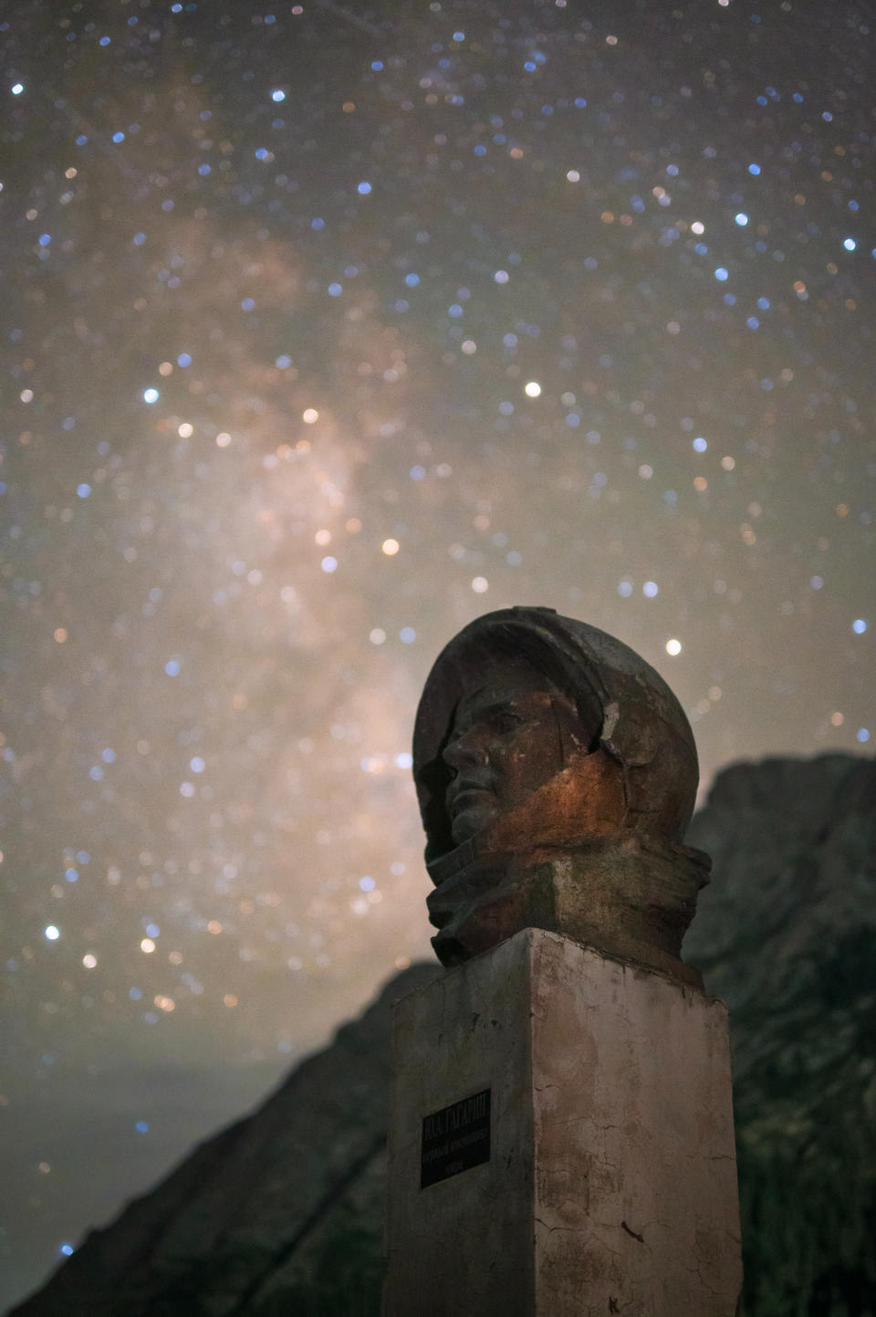 A statue of Yuri Gagarin with the milky way behind him, the sky is full of stars.